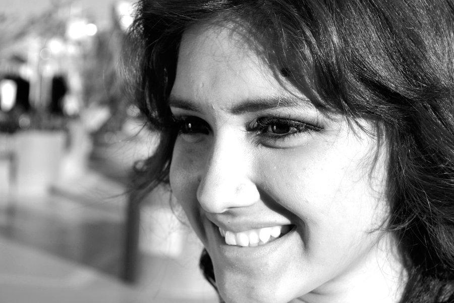 Seguridad y bienestar al desarrollar la asertividad Primer plano en blanco y negro del rostro de una mujer joven que sonríe con expresión tranquila, simbolizando la seguridad y el bienestar que aporta la asertividad.