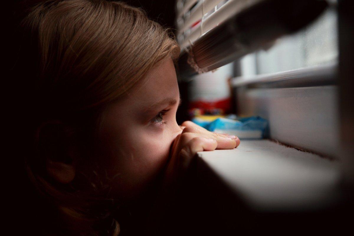 niña con miedo mirando por la ventana en confinamiento por coronavirus